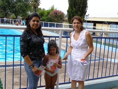María Victoria Hormazabal entrega material de difusión a un niña con su madre.