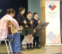 En la fotografía aparecen tres niñas cantando y junto a ellas una mujer que toca la guitarra