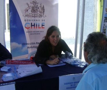 La profesional de apoyo del SENADIS, Jocelyn Franco entregado información a una persona en el stand institucional.